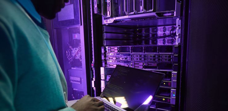 Ingénieur de données afro-américain tenant un ordinateur portable tout en travaillant avec un superordinateur dans la salle des serveurs